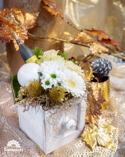 Composition florale du Nouvel An en blanc et or, avec fleurs blanches, feuillages dorés et décoration festive.